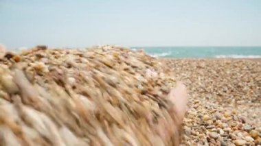 Sand and small stones through your fingers. On the beach, close-up. The sea in the background.