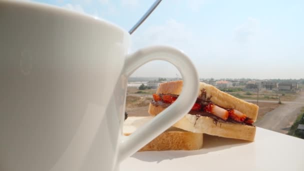 晴れた朝にはバルコニーの青空の下で朝食 カメラはマグカップを通してチョコレートとフルーツのサンドイッチにパンします ドリースライダー極端なクローズアップ ラオワ プローブ スローモ — ストック動画