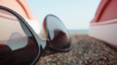 Things on the beach by the sea. Through pink flip flops and sunglasses and a red apple. Dolly slider extreme close-up. Laowa Probe.