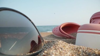 Things on the beach by the sea. Through pink flip flops and sunglasses and a red apple. Dolly slider extreme close-up. Laowa Probe.