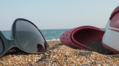 Things on the beach by the sea. Through pink flip flops and sunglasses. I put a bitten apple. Dolly slider extreme close-up. Laowa Probe.