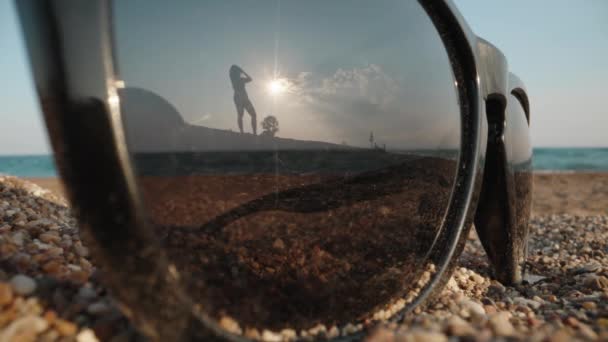 Een Zonnebril Ligt Het Zand Tegen Achtergrond Van Zee Jonge — Stockvideo