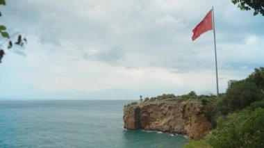 Deniz kıyısındaki yüksek bir kayanın üzerinde büyük bir Türkiye bayrağı. Deniz manzaralı. Antalya