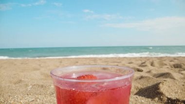 Red cocktail on the beach against the backdrop of the sea, strawberries are spinning in a glass. close-up.