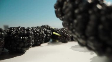 Mulberries fall on a white table. Blue sky. Summer, sunny weather. Dolly slider extreme close-up. Laowa Probe. Slow mo