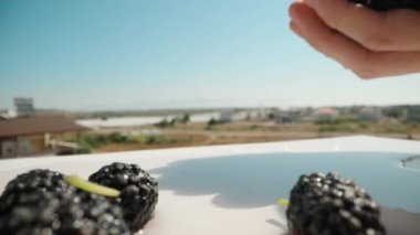 Mulberries are on the table. Strawberries fall from above. Blue sky. Summer, sunny weather. Dolly slider extreme close-up. Laowa Probe. Slow mo