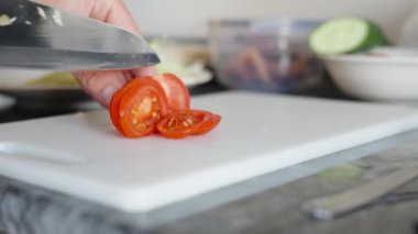 Pişirirken, domatesi büyük bir bıçakla ince dilimlere ayırdım, yakından hareket ederek. Siyah taş tezgah. Beyaz kesme tahtası.