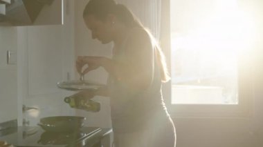 Yemek pişirmek. Yağı kızartma tavasına döküyorum. Pencerede güneş ışığı var. Hareket halinde.