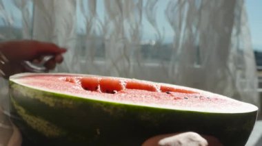 Güneşte büyük sulu bir karpuz, genç kadın kaşığı içine sokar, etrafa su sıçratır. Yakın plan.