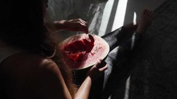 年轻的女人坐在地板上 拿着一个大西瓜 用勺子吃 西瓜在阳光下 — 图库视频影像