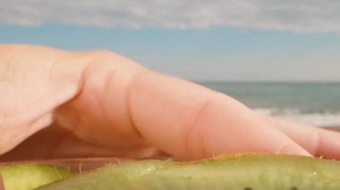 Kivi tabakta yatar, kamera yarım kivinin üzerinde döner. Kaşıkla hamuru yerim. Deniz manzaralı. Dolly kaydırıcı aşırı yakın çekim.