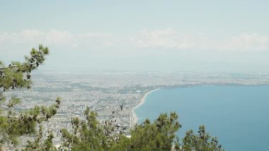 Dağın tepesinden şehir ve deniz manzarası. Çam ağaçlarının tepelerinden. Yaz, güneşli gün.