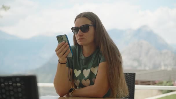Молодая Женщина Сидит Кафе Открытом Воздухе Смотрит Телефон Ветер Дует — стоковое видео