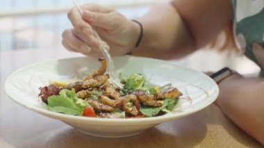 Kocaman bir tabak tavuk salatası. Genç kadın yaprakları çatalla alıyor ve yiyor. Bir kafede yaz yemeği. Hareket halinde.