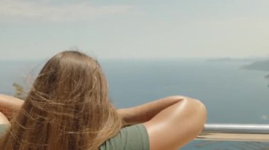 Korkulukta genç bir kadın duruyor. Uzağa bakıyor. Deniz ve etrafındaki dağlar. Yaz, tatil. Hareket halinde.