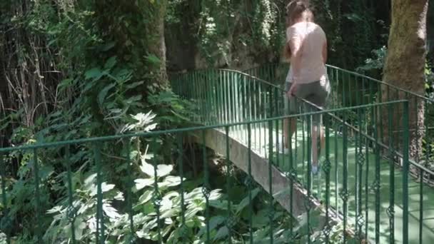 一个年轻的女人走过桥 从后面看 四周全是石头和树木 夏天散步 — 图库视频影像