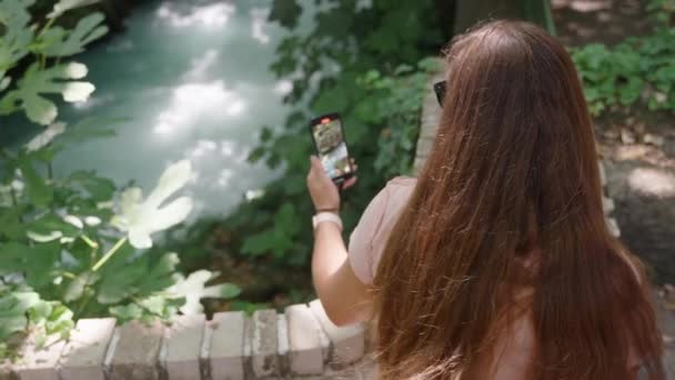 Młoda Kobieta Siedzi Kamiennej Ławce Strzela Górską Rzeką Przez Telefon — Wideo stockowe