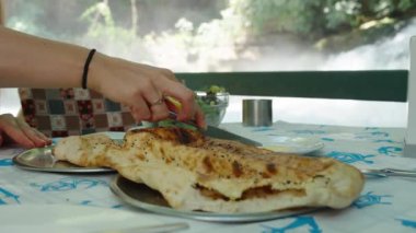 Genç kadın ekmeğin üzerine tereyağı sürer. Ekmeğin diğer ucunda bir sinek oturuyor. Bir şelalenin zeminine karşı. Yakın plan..