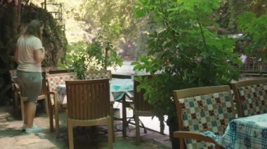 Genç bayan masada oturmaktadır. Suda bir kafe. Dağ nehrine bakıyor. Güzel doğa..