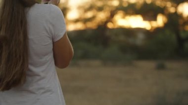 Genç kadın telefonda ateş ediyor ve Lagurus 'un çalılarını koparıyor. Gün batımında, sıcak bir ışık. Hareket halinde.
