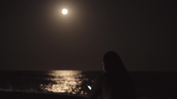 Young Woman Sits Sea Beach Looks Smartphone Moonlight Water Back — Stock Video