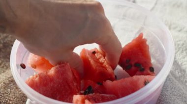 Plajdaki plastik bir konteynırdan karpuz parçaları alıyoruz. yakın plan