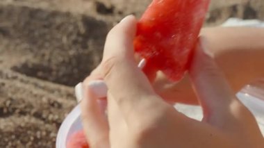 Güneş kremi sürmüş genç bir kadın sahilde uzanıyor ve karpuz parçaları yiyor. Yaklaş, ağır çekim.