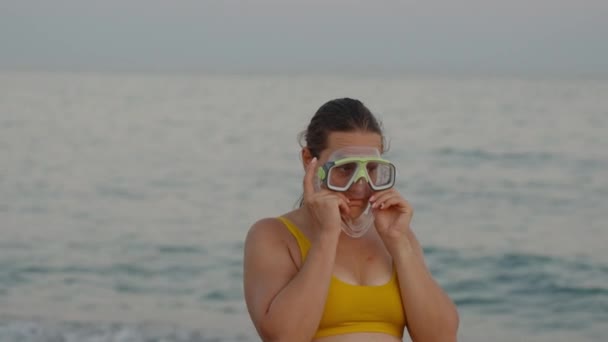 ぽっちゃり若い女性は 夕日の空と海の背景にスキューバダイビングマスクをしようとします — ストック動画