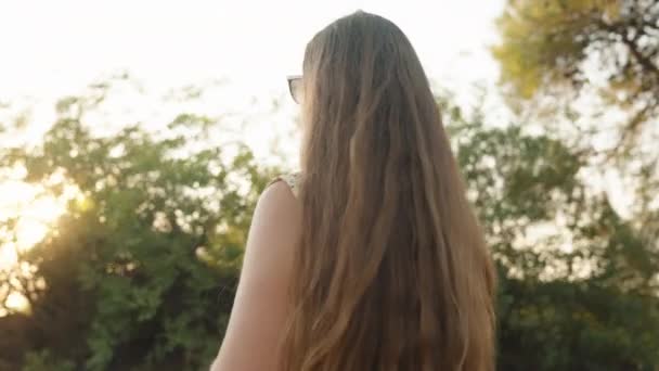 一个戴太阳镜的年轻女子站在树后喝水 夕阳西下3 摄像机在她的周围旋转 — 图库视频影像