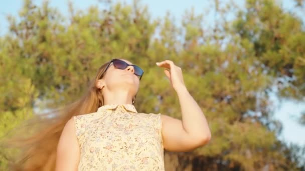 Młoda Kobieta Okularach Przeciwsłonecznych Stoi Tle Drzew Prostuje Włosy Zachodzie — Wideo stockowe