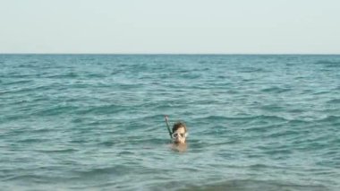 Dalgıç maskeli bir adam dalgalarda sallanıyor, sadece kafası yüzeyde görünüyor. Kameraya bak..