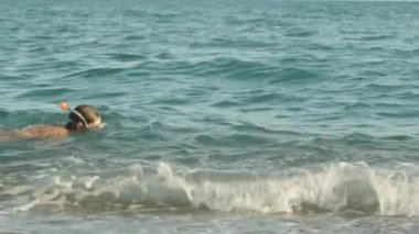 Dalgıç maskeli bir adam dalgalarda yüzer, ağır çekim.