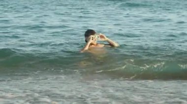 Dalgıç maskeli bir adam onu çıkarır ve güneşe bakar. Yavaş çekim