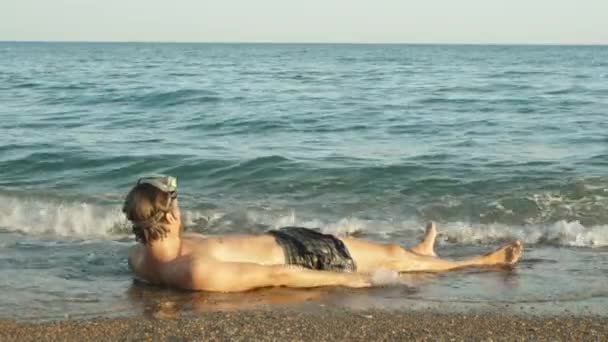 一个戴着潜水潜水面具的男人躺在海滨 双手张开 被波浪覆盖着 — 图库视频影像
