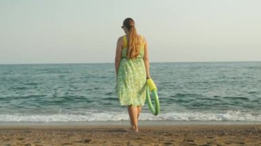 Yüzmek için köpük çemberli yeşil elbiseli tombul bir kadın denize gider.