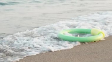 Yüzmek için yeşil bir köpük çemberi, bir deniz dalgası tarafından kıyıya vurulur..