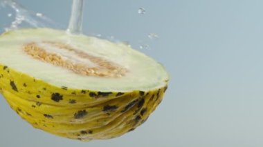 Kemikli sarı bir kavunun yarısı, üzerine su dökülür, mavi gökyüzüne karşı, yakın çekim, ağır çekim