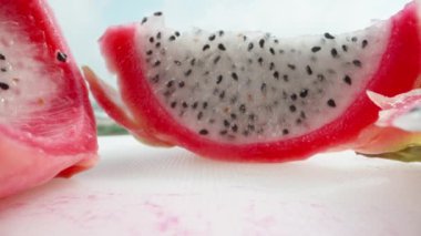 Pitahaya ya da beyaz ve kırmızı etli ejderha meyvesi, parçalara ayrılmış. Meyve suyu beyaz bir masada. Dolly Slider aşırı yakın çekim. Laowa Sondası