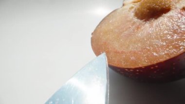 Kırmızı erik dilimleri ve onları kesen bıçak, beyaz arka planda, Dolly sürgülü aşırı yakın çekim.