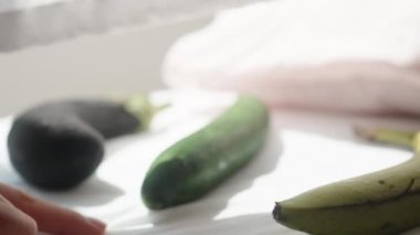 Genç kadın yatağa oturur ve patlıcan, salatalık ve muz arasında seçim yapar, ıslanırlar, muz seçer. Güneşli bir sabah, pencereden gelen ışık beyaz yatağa düşüyor. Hareket halinde