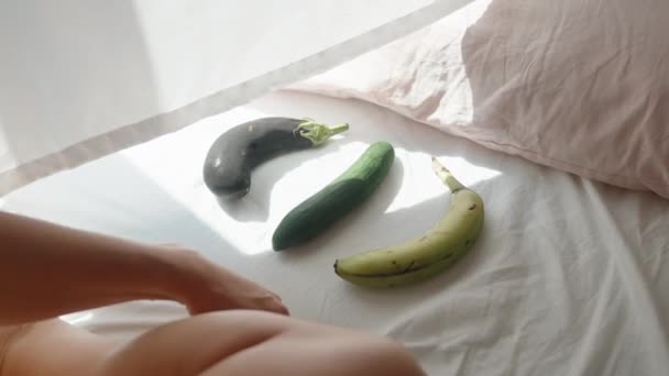 Jonge Vrouw Zit Het Bed Kiest Tussen Aubergine Komkommer Banaan — Stockvideo