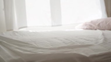Güneşli bir sabah, pencereden gelen ışık beyaz yatağa düşer, rüzgar perdeleri savurur. Yatağa pembe bir yastık atıyorum, ağır çekimde..