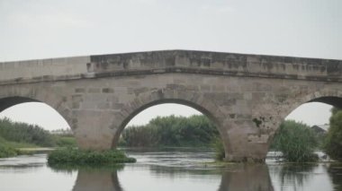 Üç kemerli tuğla köprü, nehrin karşısında. Suda yaz otları.