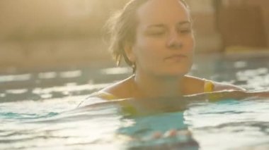 Havuzda genç bir kadın, kenara doğru yüzüyor, başını eğiyor ve dilini gösteriyor, yakın çekim, yavaş çekim.