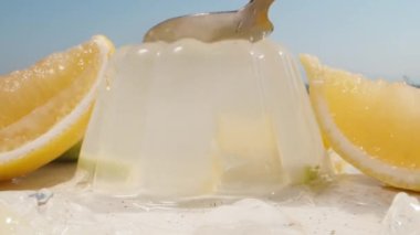 Limon dilimli bir tabakta limon jölesi. Bir kaşıkla vuruyorum ve sallanıyor. Güneş ve mavi gökyüzü. Yakın plan.