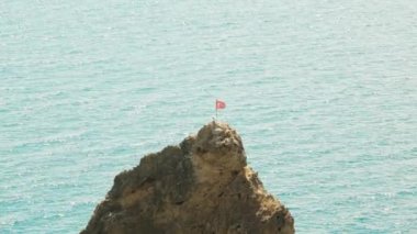 Deniz kıyısındaki bir uçurumun tepesinde bir martı. Türk bayrağı kayanın üstünde.