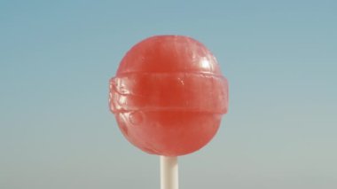 Kırmızı yuvarlak bir lolipop, gökyüzüne karşı dönüyor. Yakın plan.