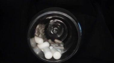 İçinde haplar olan siyah bir kavanoz. Kapsüller, dönüşler, haplar kavanozdan dökülüyor. Yakın plan..