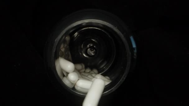 在一个旋转的黑色罐子中的白色胶囊中的片断 他们从罐子里掉了出来 黑色背景 慢动作 — 图库视频影像