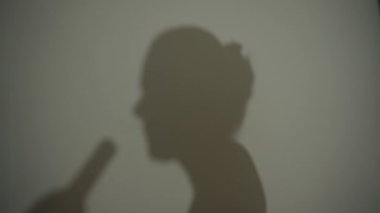 Beyaz duvarda bir gölge, şişeden şarap içen genç bir kadın..